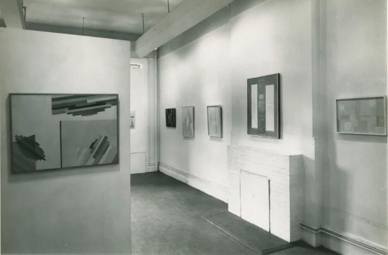 Alice Trumbull Mason’s solo show at Hansa Gallery in New York, 1959. Black and white photograph of the interior of a white-walled gallery space, with abstract paintings hung on the walls.